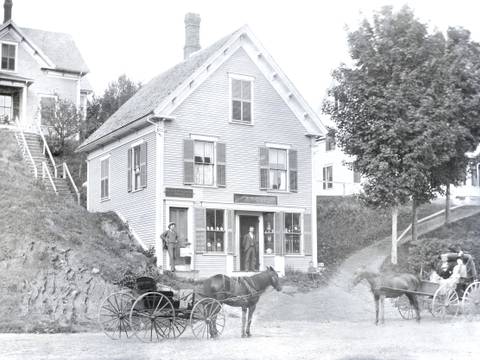 Auch ein Ort in New England: Straßenszene in Vermont, 1905 – Straße mit Haus mit Ladenfront, davor zwei Männer und zwei Fuhrwerke mit Pferden