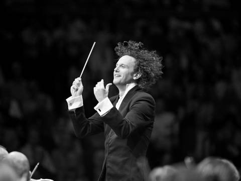 Nicholas Collon, Chefdirigent des Finnish Radio Symphony Orchestra – Ein Mann mit locken Haaren und einem Taktstock in der Hand dirigiert so überschwänglich, dass seine Haare herumwirbeln.