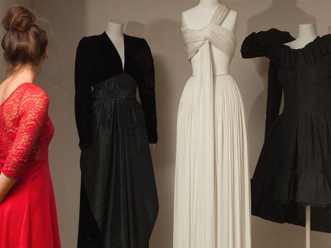 Blick in die Modegalerie – Person in rotem Kleid betrachtet drei Schaufensterpuppen in schwarzem und cremefarbenem Kleid. Fotografie.