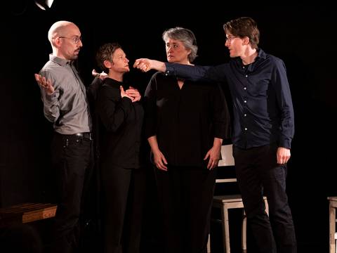 Theater ohne Probe TOP – Vier Personen auf einer Bühne in schwarzer Kleidung. Eine Person zeigt mit dem Finger auf eine andere, alle blicken konzentriert.