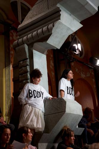Foto: Lee Everett Thieler – Zwei Personen lehnen an einer steinernen Struktur, tragen weiße Shirts mit der Aufschrift "BODY". Weitere sitzende Personen unten im Bild.
