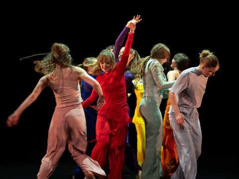 find no words to say – Personengruppe in farbenfroher Kleidung tanzt dynamisch auf dunkler Bühne.