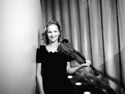 Die Violinistin Hilary Hahn – Eine Geigerin steht an der Wand gelehnt und schaut in die Kamera.