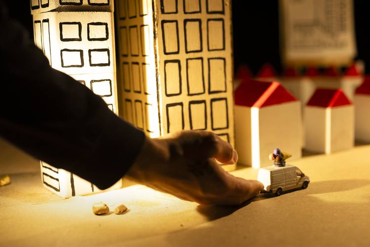 Plateau – Hand bewegt weißen Spielzeugwagen in Miniaturstadt mit hohen Gebäuden und kleinen Häusern mit roten Dächern.