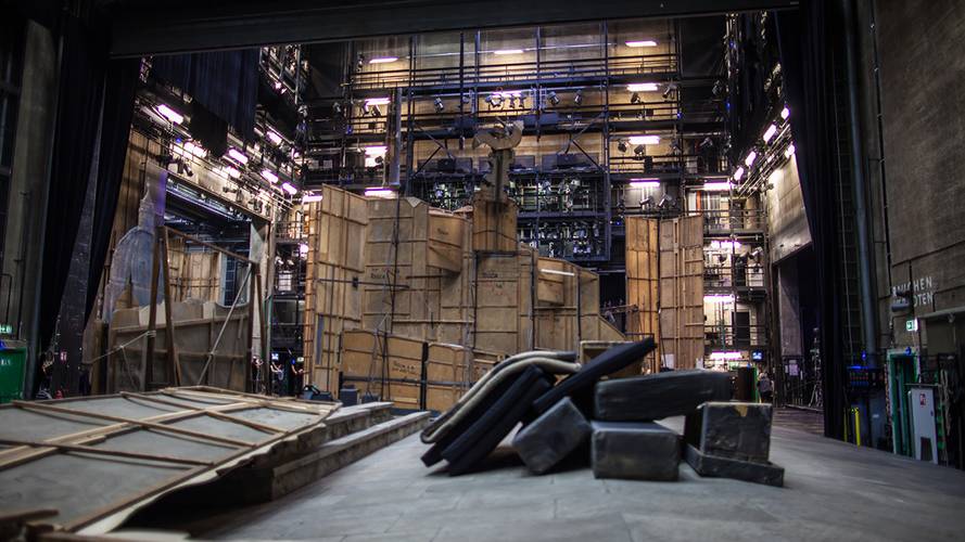 Backstage-Führung – Buehnenbau mit Holzwänden und Requisiten auf einer Theaterbühne, umgeben von Beleuchtung und technischen Anlagen.