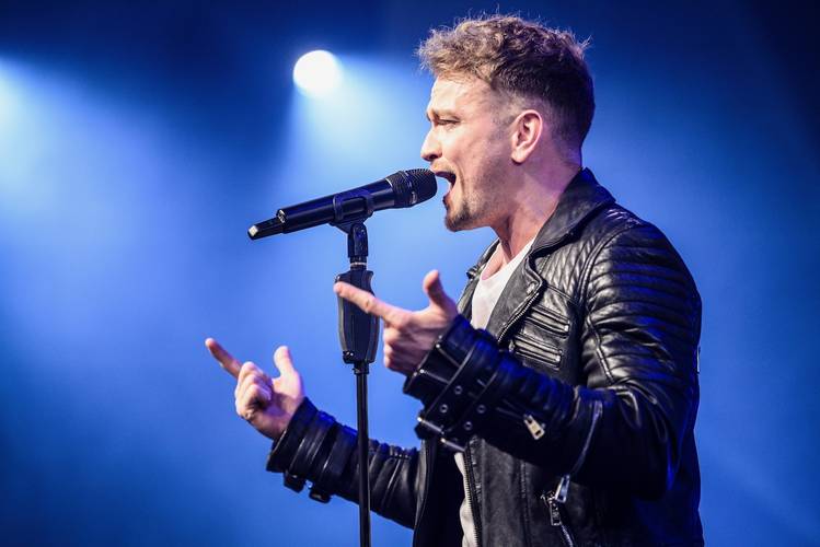 BEATHOVEN – Beat für Elise – Person mit Mikrofon, schwarze Lederjacke, singt auf einer Bühne, blauer Hintergrund mit Bühnenlichtern.