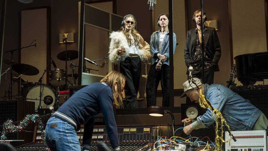 Stereophonic – Fünf Personen in einem Aufnahmestudio, vier stehen, eine kniet; Mischpult mit Kabeln, Schlagzeug und Klavier im Hintergrund, Kopfhörer tragen.