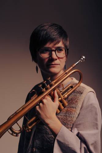 Laura Jurd – Person mit einer Trompete in der Hand vor grauem Hintergrund.