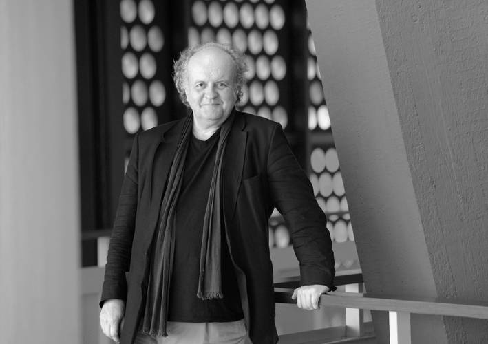 Der Komponist Wolfgang Rihm 2021 in der Philharmonie Berlin – Ein Mann in Jacke und Schal lehnt an einem Geländer im Foyer der Philharmonie.