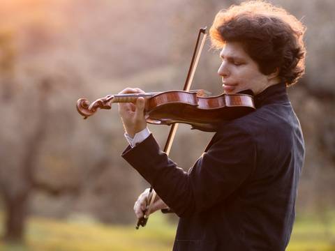  – Augustin Hadelich spielt im freien Geige, Bäume im Hintergrund
