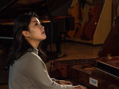 Hyunji Kim – Person an einem Flügel sitzend, spielt Klavier. Im Hintergrund weitere Musikinstrumente.