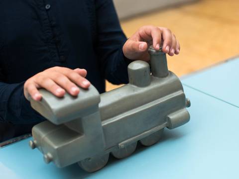 Die Form einer Lokomotive an einem Modell ertasten. – Hände ertasten das Modell einer Lokomotive.
