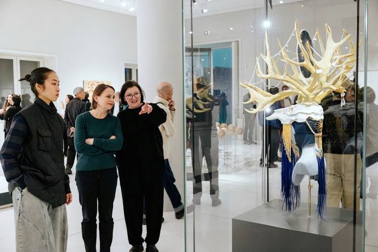 Eröffnung der Wechselausstellung "Sich verwandt machen" – Drei Personen bewundern ein kunstvolles Objekt in einer Galerie, umgeben von anderen Besuchern.