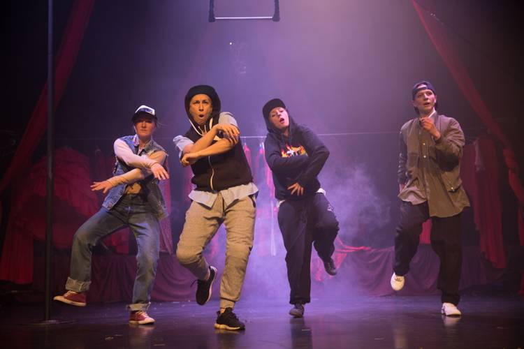 Barbaren Barbies: A wild women circus – Vier Personen tanzen energisch auf der Bühne. Nebel im Hintergrund, rote Vorhänge sichtbar. Alle tragen lässige Streetwear und Mützen.