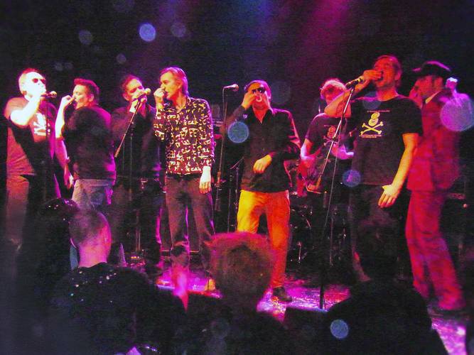 Das Original Oberkreuzberger Nasenflötenorchester – Eine mehrköpfige Band singt und performt live auf einer Clubbühne unter buntem Scheinwerferlicht