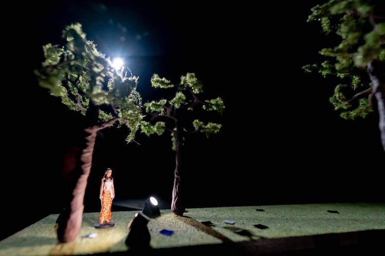 Transport: Fasten your Seatbelts! – Miniatur-Figur einer Person unter Bäumen mit einem Spotlicht auf sie gerichtet, im Hintergrund dunkler Raum.