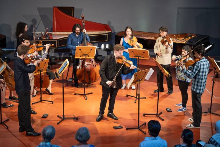 Personal Note Konzertreihe , Barenboim-Said Akademie; Foto: Peter Adamik – Gruppe von Musiker*innen spielt mit Streichen und einem Kontrabass in einem Raum mit rotem Boden, Harpsichord und Flügel im Hintergrund.