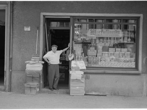 Winsstraße, 1055 Berlin, 1975 – Schwarz/ Weiß Fotografie Mann in der Tür eines "Seifen - Parfümerien Wirtschaftswaren" Geschäfts. Frontalansicht des Ladens mit Schaufenster