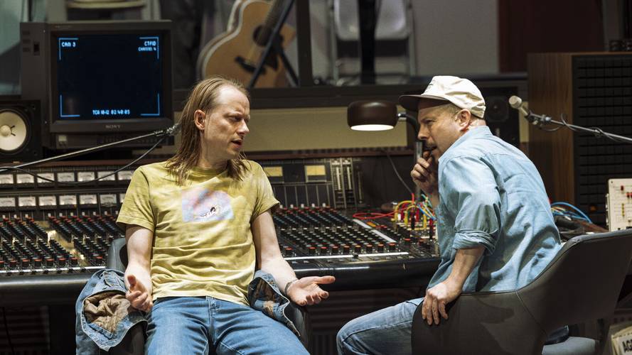 Stereophonic – Zwei Personen in Tonstudio sitzen an Mischpult, diskutieren. Person links trägt gelbes Shirt, Person rechts trägt Basecap, hält Hand an Gesicht.