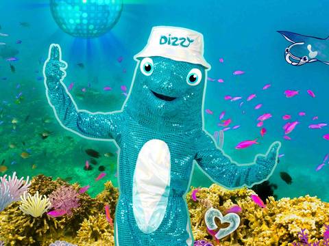  – Ein blauer Fisch-Maskottchen mit Hut "Dizzy" unter Wasser, umgeben von Fischen, Korallen und einer lila Discokugel. Rechts ein Rochen.