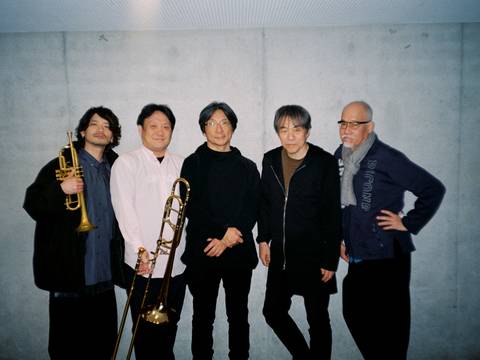 Otomo Yoshihide New Jazz Quintet – Fünf Personen stehen vor einer grauen Wand; zwei halten Instrumente, eine Trompete und eine Posaune.