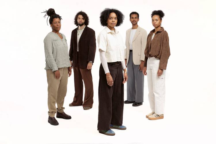 Neneh Boye & Band – Fünf Personen stehen nebeneinander auf weißem Hintergrund. Alle tragen lässige Anzüge und Hemden.