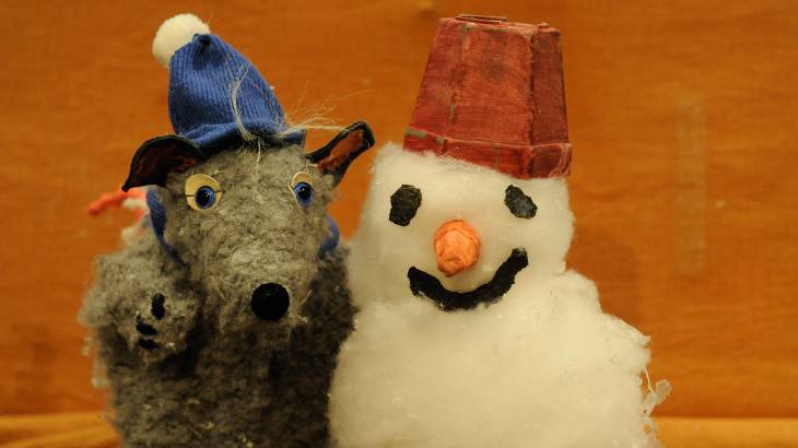 Schneeschön und Bitterkalt – Eine graue Stoffmaus mit blauer Mütze neben einem Schneemann mit rotem Hut und Karottennase, beide auf orangenem Hintergrund.
