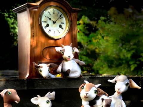 – Sechs Plüschziegen vor einer antiken Standuhr mit römischen Ziffern im Freien.
