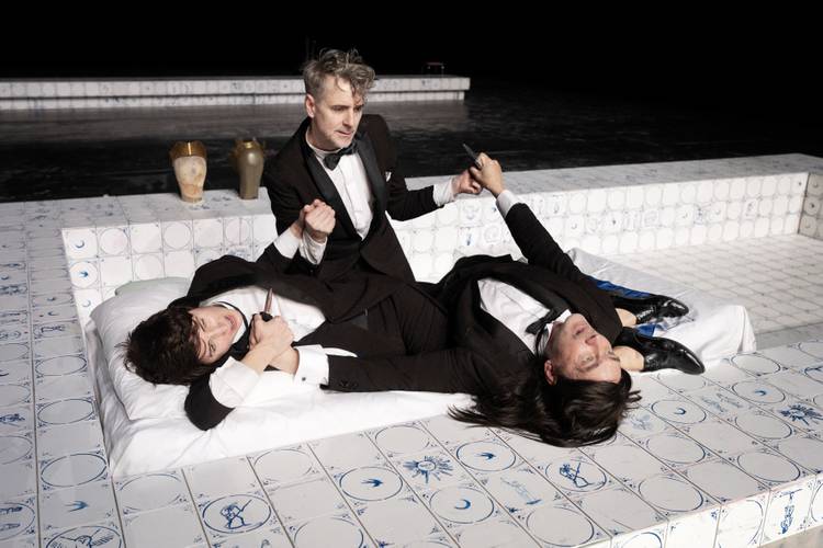 Macbeth – Drei Darsteller*innen in Anzügen sind auf einer Matratze in einem gefliesten Becken