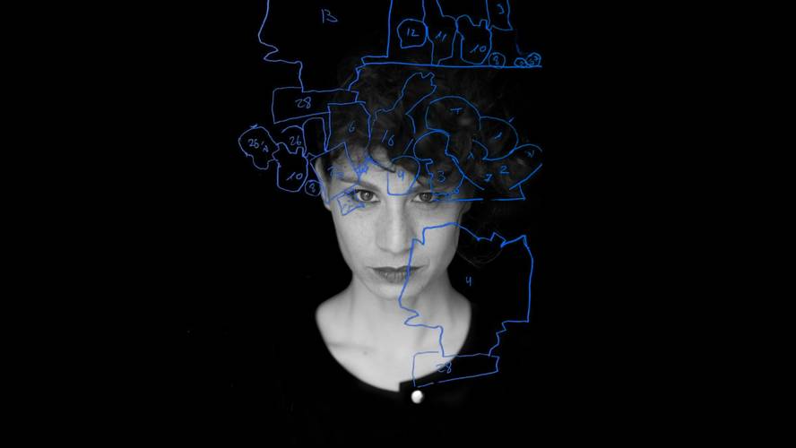 À la carte – Person mit kurzen Locken, das Gesicht zur Haelfte beleuchtet. Blaue Skizze mit Zahlen ueber dem Gesicht auf schwarzem Hintergrund.