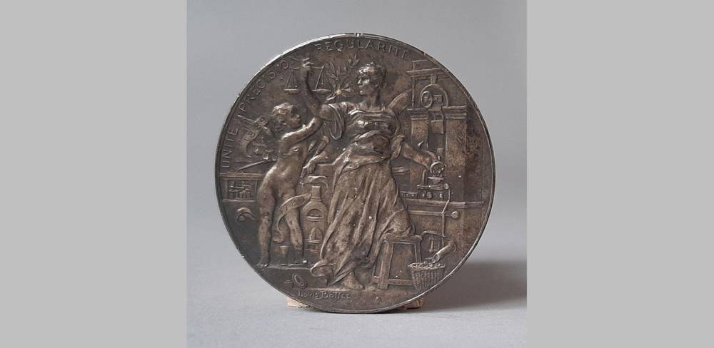 Louis-Alexandre Bottée: Medaille „Darstellung der Justitia an einer Geldprägemaschine“ – Silberne Medaille mit geprägten Figuren. Person sitzt, hält Waage. Text: "UNITÉ PRECISION REGULARITÉ".