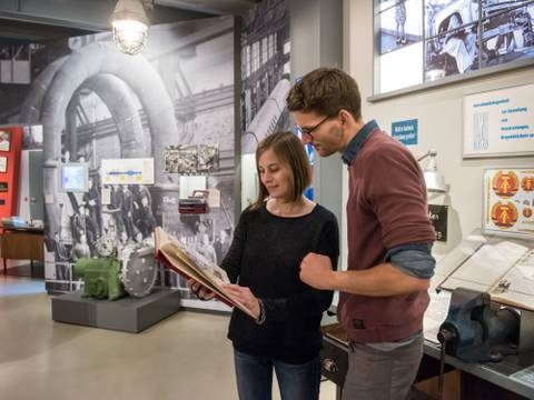Dauerausstellung "Alltag in der DDR" – eine Frau und ein Mann betrachten gemeinsam eine Mappe mit Dokumenten aus der Ausstellung "Alltag in der DDR"