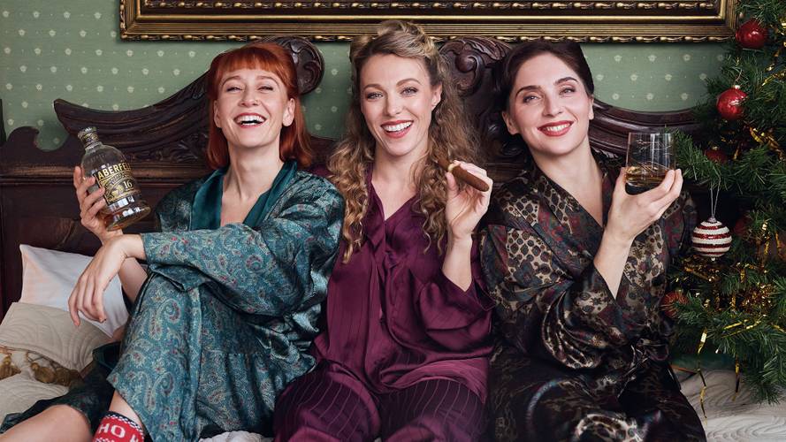 The Airlettes: Underneath the Mistletoe – Drei lachende Personen in Pyjamas, die Whisky trinken. Die linke Person haelt eine Flasche mit der Aufschrift "ABERFELDY 16". Ein Weihnachtsbaum rechts.