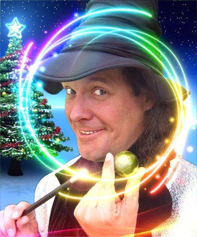 Person mit schwarzem Hut, Zauberstab und grüner Kugel in der Hand. Helle Lichtringe umgeben die Person. Im Hintergrund ein Weihnachtsbaum mit Stern.