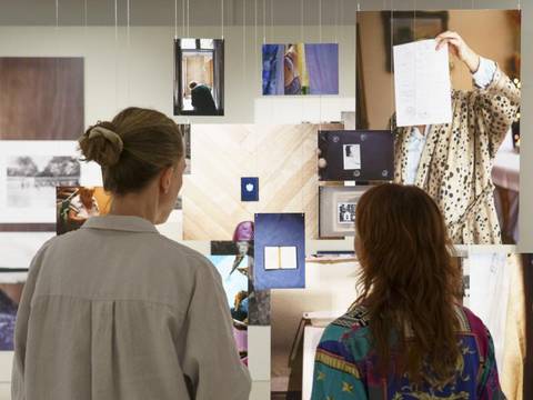  – Zwei Besucherinnen sehen sich Fotografien in der Ausstellung an und sind von hinten zu sehen.