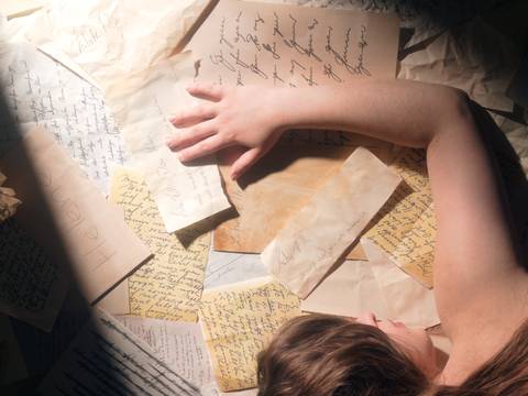  – Person mit ausgestrecktem Arm liegt auf handschriftlichen Briefen und Zetteln, einige vergilbt. Umschlag mit Aufschrift "Helene" sichtbar.