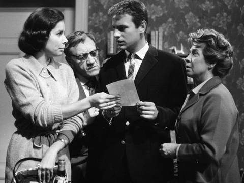  – Vier Personen in den 1960er Jahren, die sich unterhalten und ein Blatt Papier betrachten.Show image caption