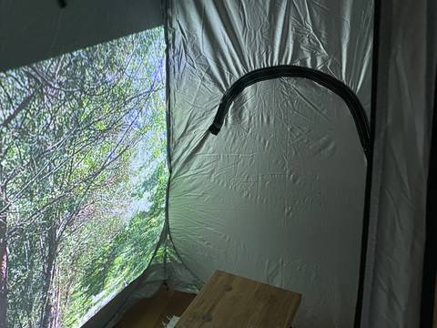 Einfach mal nichts tun. – Das Bild zeigt einen kleinen zeltartigen Raum mit silbernen Wänden. An eine Wand ist ein Foto von grünen Bäumen projeziert. In der Mitte des Raumes steht ein Hocker aus Holz auf einem weißen Teppich.