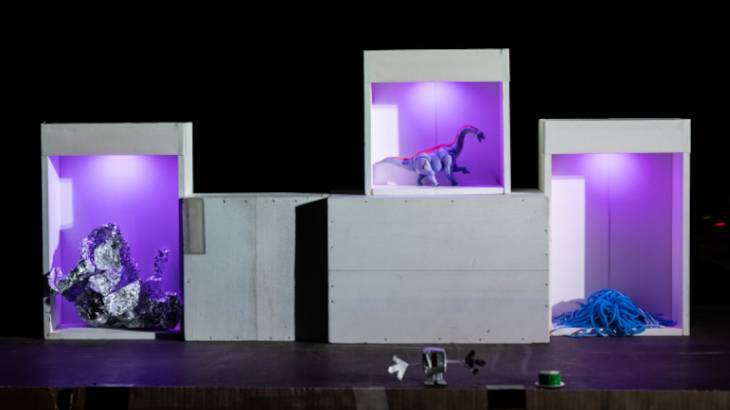 Der Viereckplanet – Drei beleuchtete Boxen mit violettem Licht. Links Alufolie, Mitte Dinosaurierfigur, rechts blaue Schnur. Unter den Boxen sind kleine Gegenstaende.
