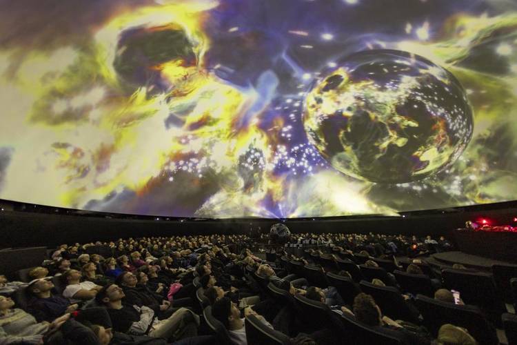 Menschen im Planetariumssaal des Zeiss-Großplanetariums und bunte Visualisierungen an der Kuppel.