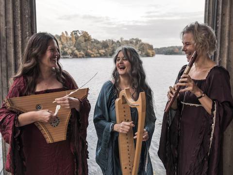 Triphonia – Berliner Ensemble für Musik des Mittelalters – Die Musikerinnen des Ensembles Triphonia mit Instrumenten in einem Pavillion am See stehend, miteinander scherzend