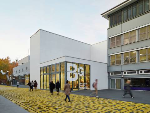 Berlinische Galerie, Außenansicht – Moderne Gebäudefassade der Berlinischen Galerie mit großen Fenstern und Beschriftung. Vorplatz mit gelbem Raster und Schrift. Menschen spazieren.