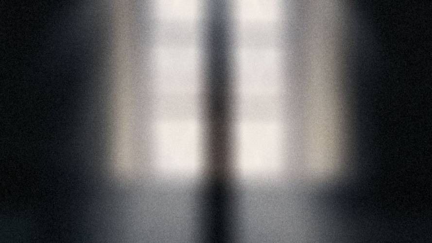 Verschwommenes Bild eines hohen Fensters mit Licht, das in einen dunklen Raum fällt.