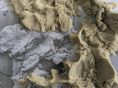  – Foto: Nahaufname von geformtem kinetischem Sand auf einer schwarz-weiß-Fotografie davon.