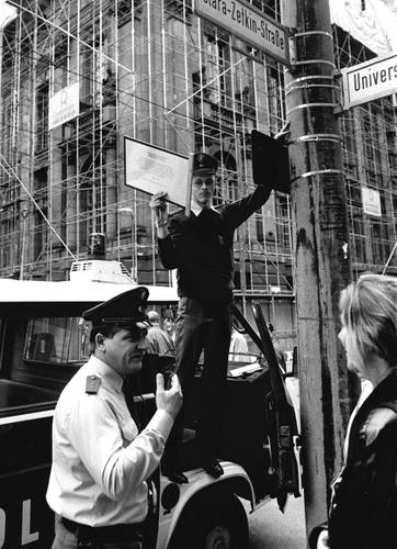 Die Polizei entfernt am 2. Oktober 1994 die vom Aktiven Museum angebrachte Zusatztafel zur Clara-Zetkin-Straße. – Schwarz-Weiß-Fotografie: Ein Polizist entfernt ein zusätzlich angebrachtes Straßenschild des aktiven Museums, während ein weiterer Beamter im Gespräch mit einer Frau steht.