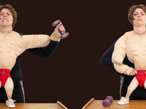 – Eine Person trägt ein Muskelkostüm mit roten Shorts. Links hebt die Person lila Hanteln, rechts macht sie eine Pose, zwei Hanteln liegen auf dem Tisch.