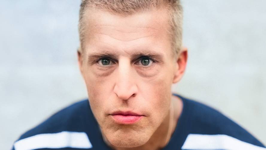 Benjamin von Stuckrad-Barre – Person mit kurzem Haar und blau-weiß gestreiftem Oberteil blickt direkt in die Kamera vor grauem Hintergrund.