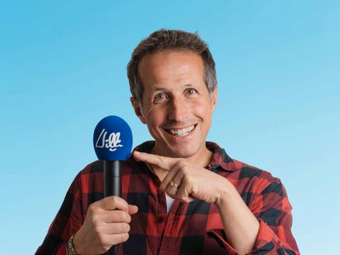  – Männlich gelesene Person mit blauem Mikrofon, darauf "will". Person trägt ein rot-schwarz kariertes Hemd und lächelt in die Kamera vor blauem Himmel.