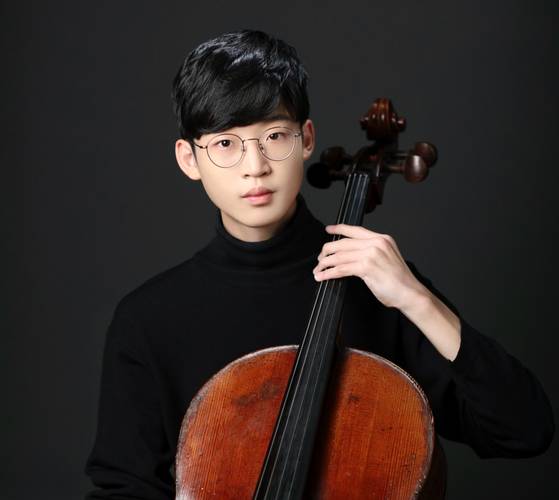 Person mit Brille und schwarzem Rollkragenpullover spielt ein Cello, vor einem dunklen Hintergrund.